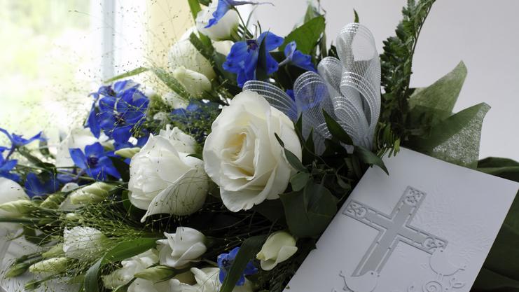 Blumenarrangement mit weißen Rosen und blauen Blüten, kombiniert mit einer tiefen Karte mit gekreuztem Motiv.