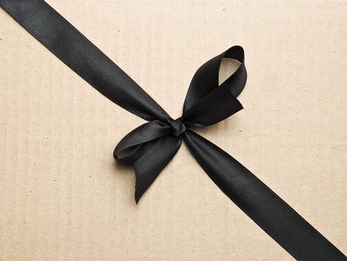 Schwarzes Satinband in einer Schleife auf einem braunen Papierkarton.