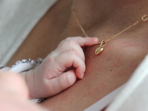 Babyhand greift sanft nach einer goldenen Halskette mit Anhänger auf der Haut einer Person.